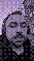 a selfie of a white person, wearing either headphones or a helmet, making an odd expression. the photo is edited to be colorized into a monochrome purple-ish color palette.